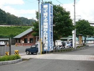 木と標語の看板に隠れた遠くの永原駅舎