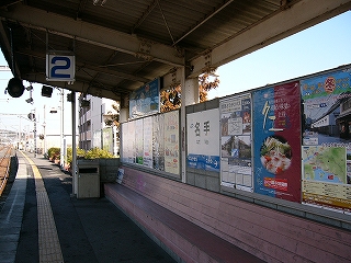 ピンクに塗られた木製の長椅子が作りつけられた開放式の待合所。背もたれはコンクリートブロックの壁でいろんな種類のポスターが貼られている。