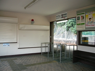 駅舎に入って斜め右を見る。左に白いシャッター２つ、角を挟んで右に改札口。床は大き目の六角形の石を敷き詰めてある。