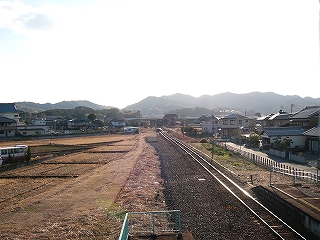 左手に土の線路跡、右手にバラストの敷かれた二線分の線路内。遠くには低い山が立ちはだかっている。