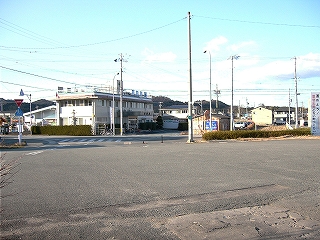 広場の向こうに道路が横切っている。その向こうに二階建ての病院の建物。