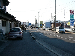 自動車の通り代わりとある道路。脇には住宅、大きな店。
