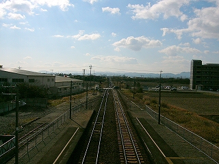 左手奥と右手奥に大きな建物があるきり、目立った建物のない風景の中、伸び続ける線路。