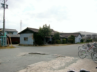 アスファルトの敷地。奥に3件の古い民家。