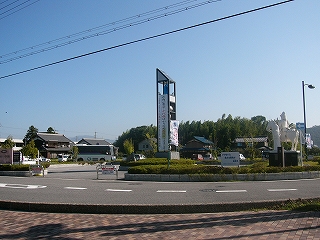手前にはカーブする道路、その隣向こうにロータリーがある。ロータリー内にある塔と白い石像が目立っている。