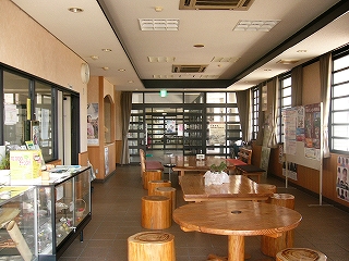 床は落ち着いた色の四角いタイル石が敷き詰められ、その上に明るい機の色のテーブルと丸太の椅子が並ぶ。奥には黒とガラスの縞々の扉。