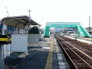 屋根のない緑色の跨線橋。写真すぐ左手にホームに作られた簡単な待合所。