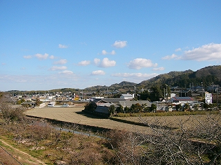 小さな川、休耕田、住宅、端の方に低山の連なり。