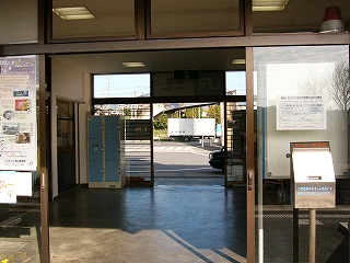 開かれた大きなサッシの引き戸の向こうに見える灰色の床面の駅舎内。もうすでに奥に駅舎の出口がすぐ見えている。