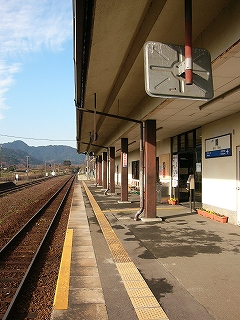 鉄筋コンクリートの建物の庇が太い鉄骨に支えられてできた回廊内のようす。右手奥に駅舎への入口があり、その前にきっぷ箱がある。