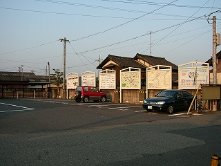 低いコンクリート塀に沿った駐車場。塀に沿わせるように大きな看板が幾つも並んでいる。