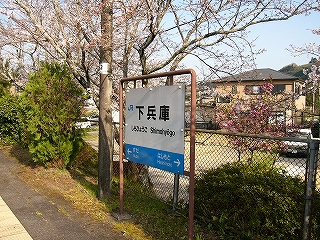 駅名標、芝生、植え込み、フェンス。