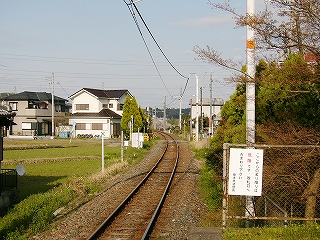 遠くで左カーブする線路。田んぼ、家。