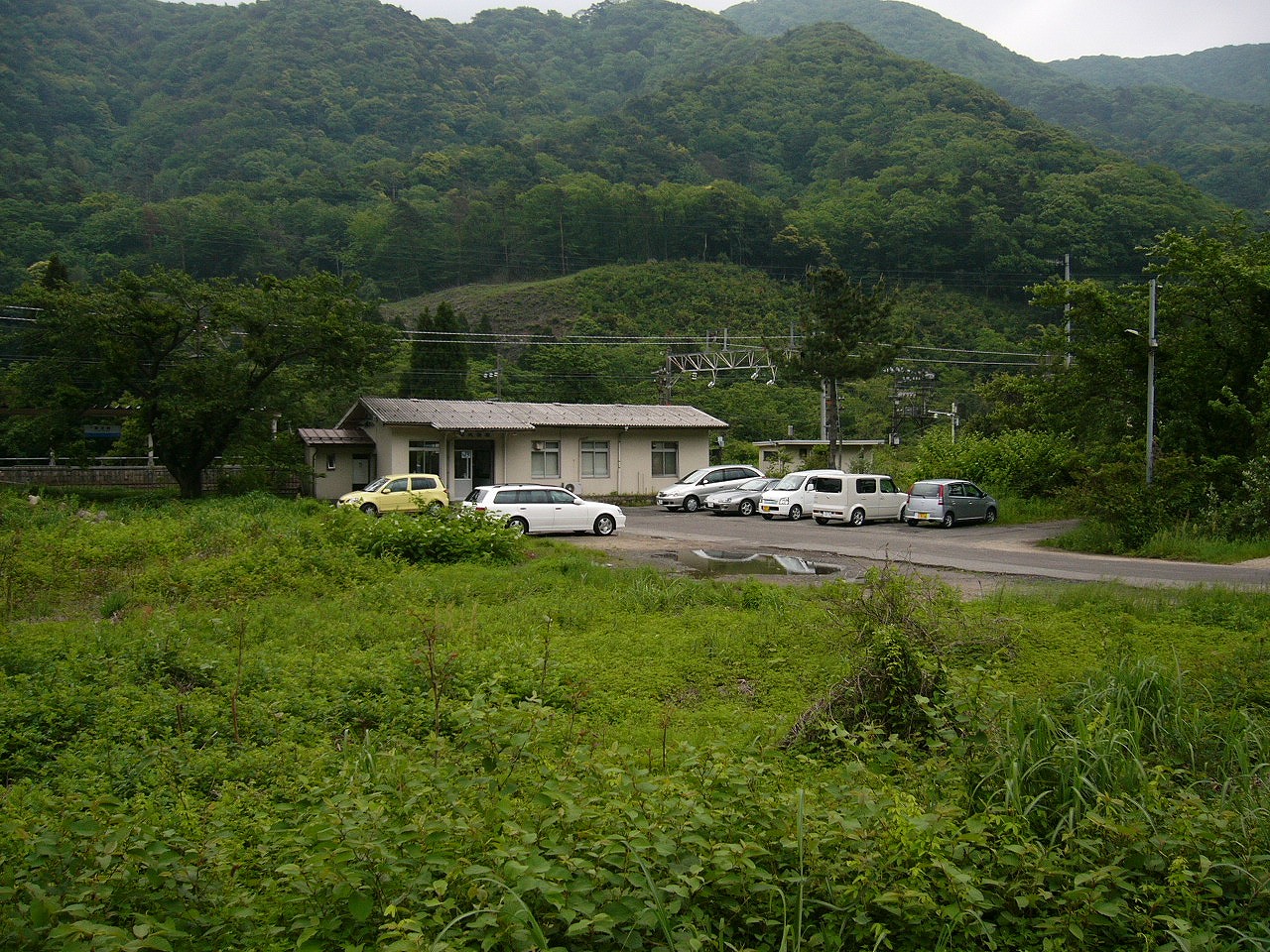白く古い感じの小さな駅舎を斜めからかなり遠巻きに見て