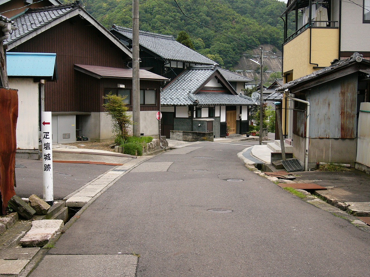 白いポールに赤字で矢印、黒字で疋壇城跡、そして田舎らしい民家。
