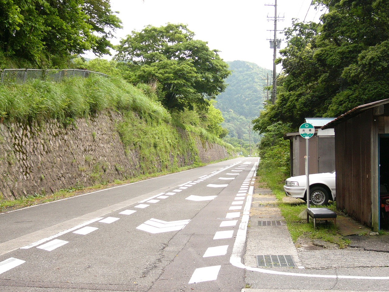 左手に山が迫り、右手に住宅がある道路とバス停。