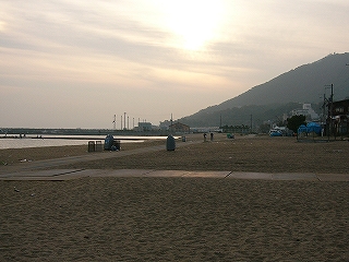 砂浜と、倉庫の間から垣間見える青い色の電車。