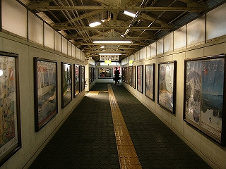 両脇にポースターが張られる跨線橋内。床が暗緑色、壁がクリーム色で全体的に薄暗い。