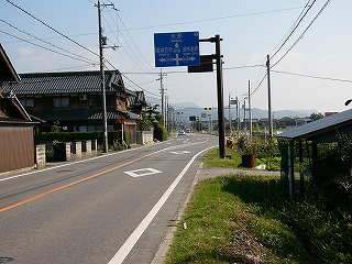 田舎らしい家と田畑、2車線の道路、青看板。