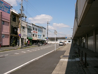人も車もほとんど通っていないに車線の道路の左脇に三階建ての古い建物の並び、右手は高架。