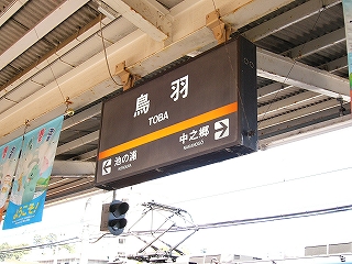 こげ茶地に白地で書かれた駅名標。オレンジのラインが入っている。