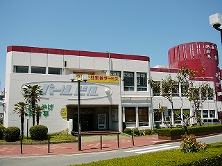 二階建ての白いビルの上辺と赤い円筒形の部分を赤色に塗った建物。