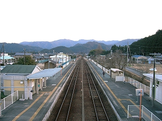 伸びゆく二線と両脇の新しい感じの上屋のないホーム。遠くにあるそれほど高くない山々がまるで伸び行く線路を阻んでいるようだ。