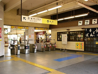 5レーンの自動改札の並びを左斜めに見て。右手に格子扉の駅そば「汽笛屋」。濃い紺色に白い毛筆体で「そばうどん」と書かれた暖簾がかかっている。