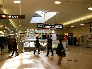 先ほどの階段の向かいにある別の階段とエスカレーターを前にして。コンコースの真中にぽっかりと口を開けたように作られたホームへの下り口。両脇は広い通路になっている。