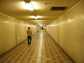 滑り止め黒ゴムつきの、黄色と白の床免罪が敷き詰められた、古めかしい地下道内。両壁は白色のレンガ風の積み重ねになっている。天井も白に近いクリーム色に塗られ、照明を反射している。