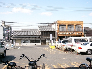 アスファルトの広い敷地。向こうに道路を挟んで低い家屋。