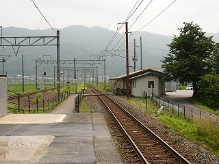 ホームの端から伸びる細い通路。線路と線路の間を通り、右に折れて踏み切りを渡り駅舎へ向かっている。