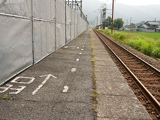 「出口」という文字と矢印が細い字でペイントされたホームのアスファルト。