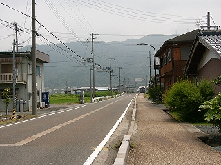 古いコンクリートの消雪装置が中央線のように見える道路。すぐ右手に人家。