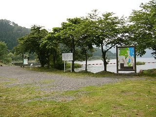 右斜めに湖岸の並木、その手前に砂利と芝生のある敷地。