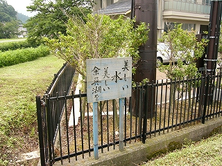 縦書きで四行に分けて黒い字で「美しい/水/美しい/余呉湖を」と書かれた、木の板が見えるぐらい極薄く水色に塗られた板の看板。